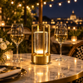 Gold cordless crystal lantern lamp glowing on a marble bistro table between wine glasses