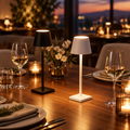 Black and white cordless dome table lamps glowing on a walnut dining table set for dinner